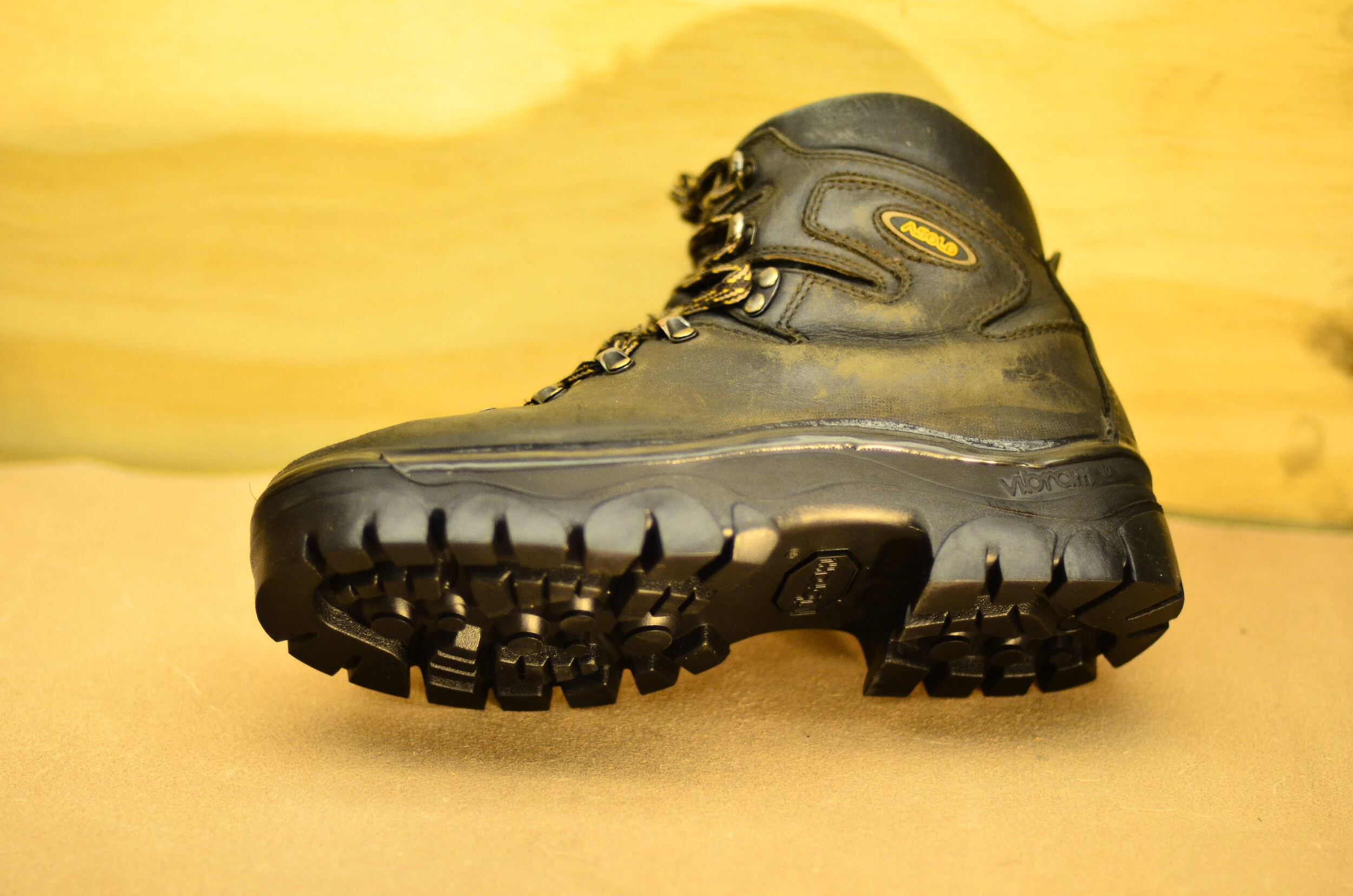 Black hiking boot viewed from underside on a yellow background.