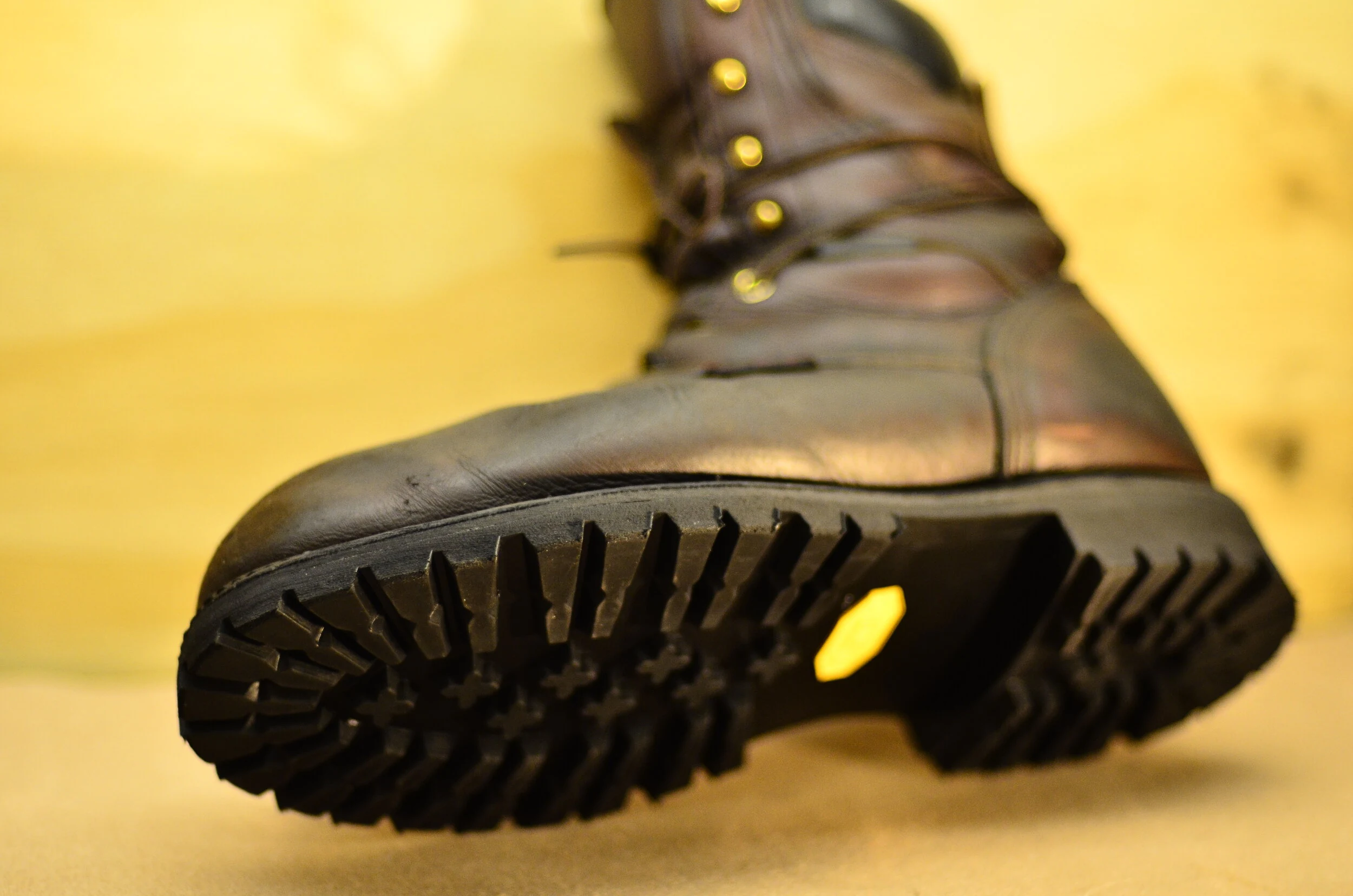 Close-up of the sole of a black leather boot with yellow background.