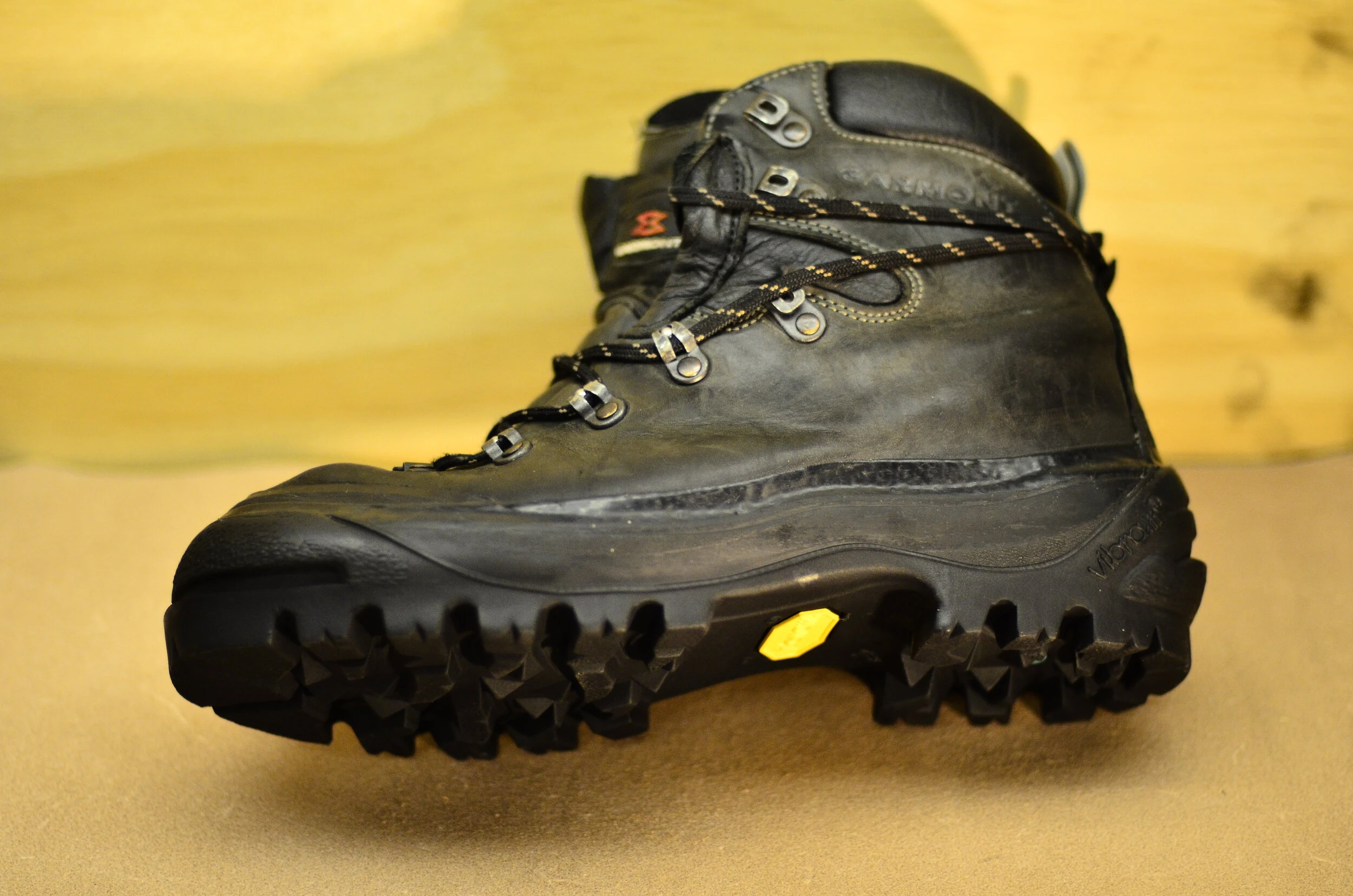 A black hiking boot with rugged sole and metal eyelets on a wooden surface.